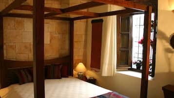 A four-poster bed with a stone wall backdrop, a bedside lamp, and a window with curtains.