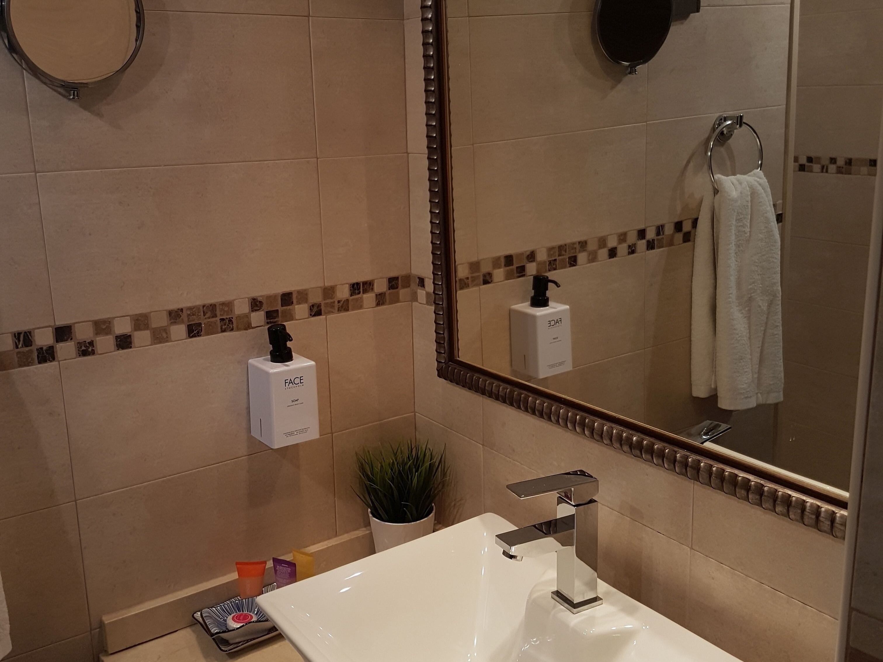 A modern bathroom with a white sink, a mirror, and a hand soap dispenser on the wall.
