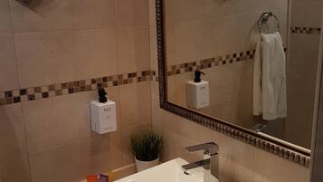 A modern bathroom with a white sink, a mirror, and a hand soap dispenser on the wall.