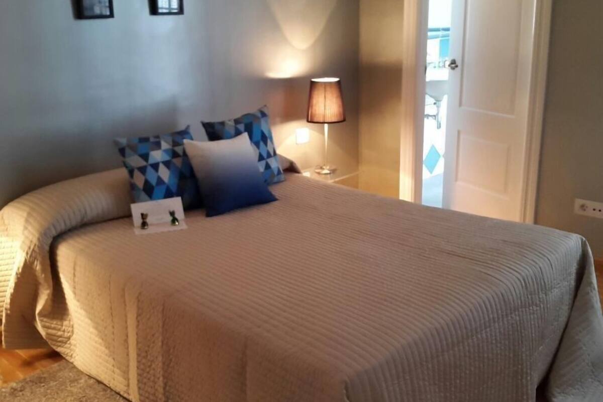 A neatly made bed with a beige comforter and pillows, a bedside lamp, and a door leading to a balcony.