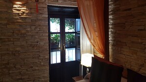 Una habitación con pared de piedra, ventana con vistas a la vegetación y una lámpara en la mesita de noche.