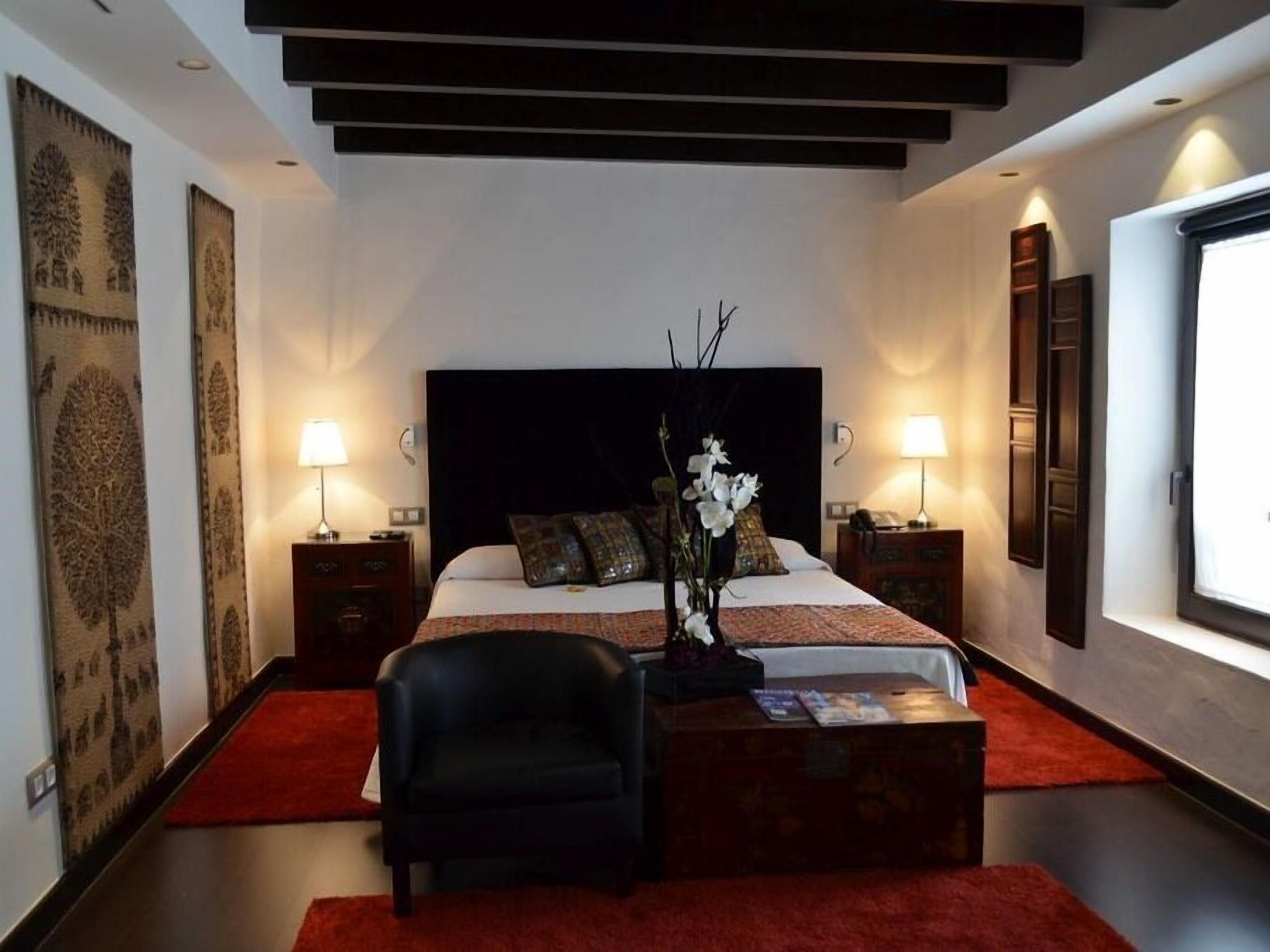 Een moderne slaapkamer met een groot bed, twee nachtkastjes, een zwarte stoel, een rood tapijt en een raam met uitzicht.