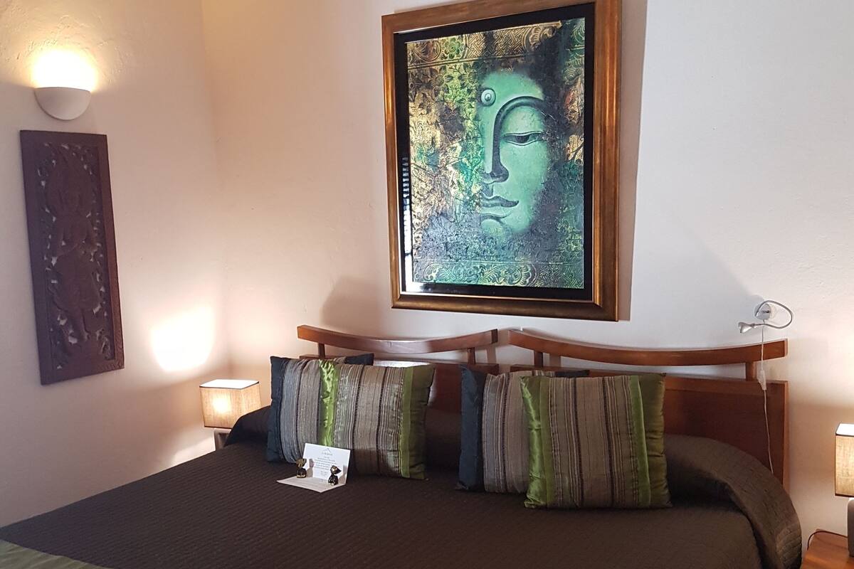 A bedroom with a bed, pillows, a framed artwork, and bedside lamps.