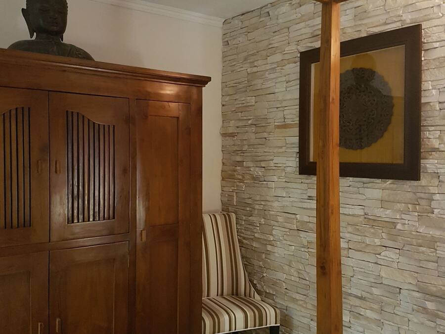 Una habitación con un armario de madera, una silla a rayas y una pared de piedra con una obra de arte enmarcada.