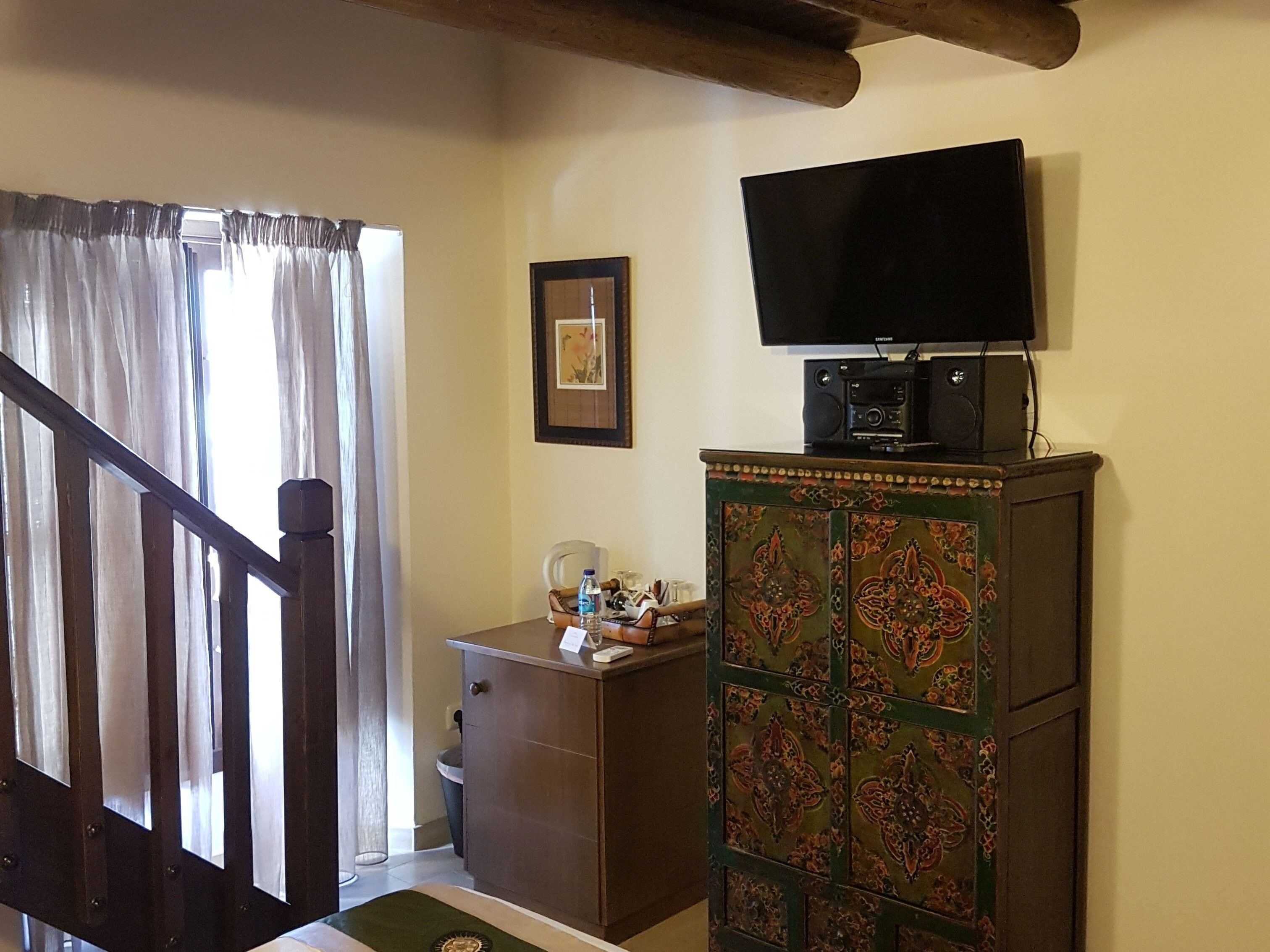 A room with a staircase, a television on a cabinet, a framed picture on the wall, and a small desk with a water bottle.