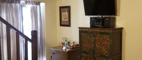 A room with a staircase, a television on a cabinet, a framed picture on the wall, and a small desk with a water bottle.