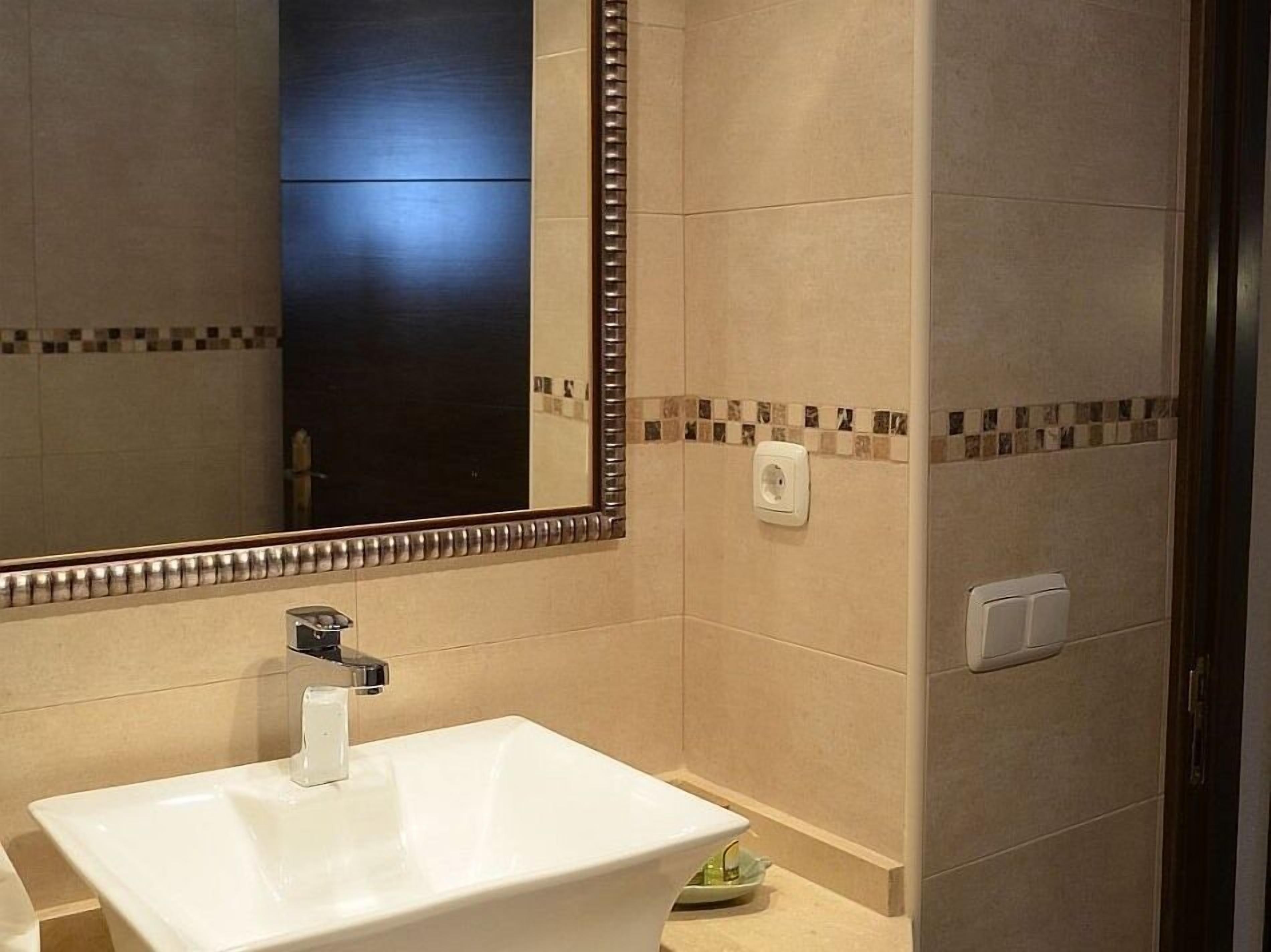 A bathroom with a white sink, a large mirror, and tiled walls.