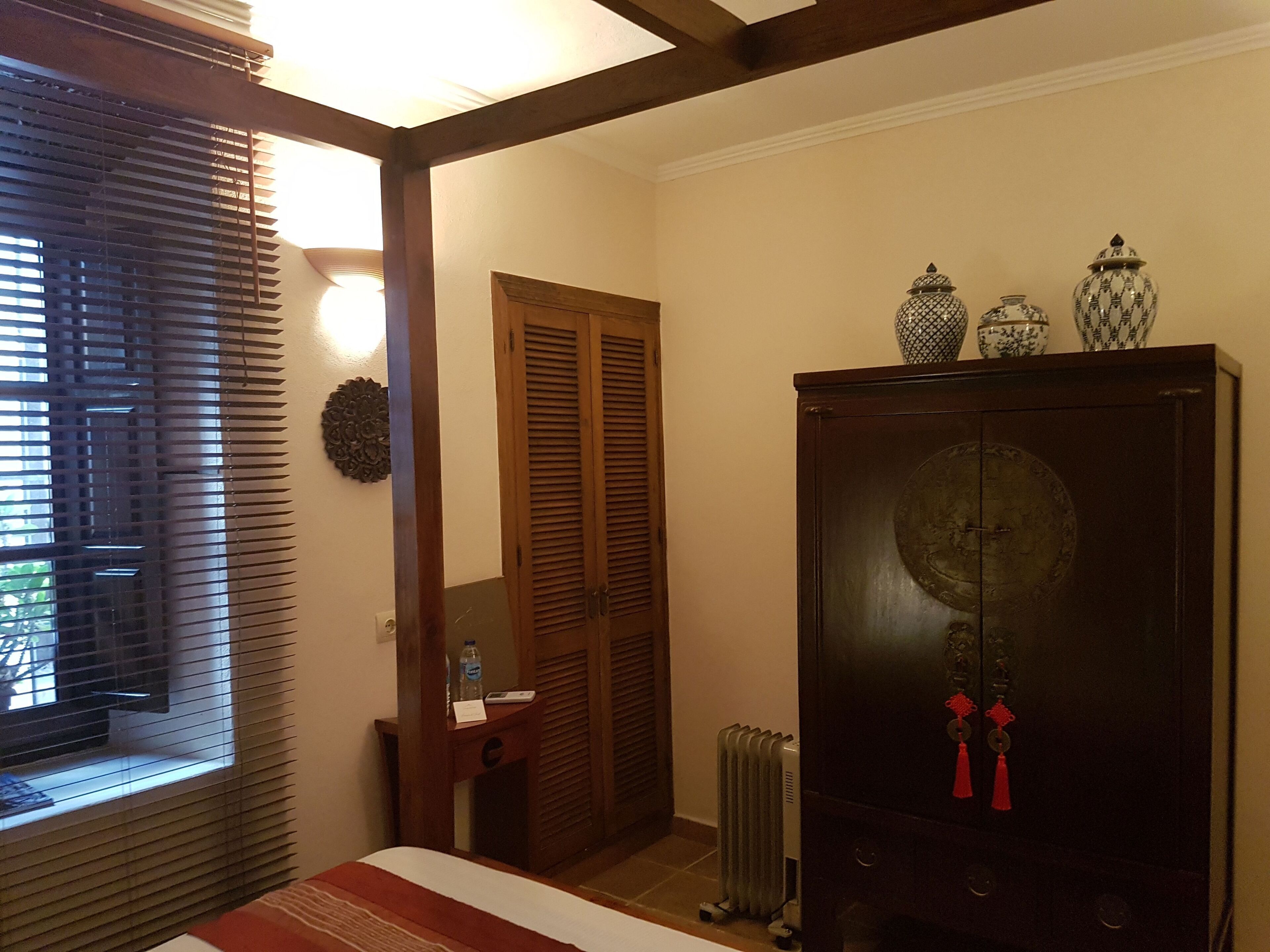 Una camera d'albergo con un letto, un armadio in legno, un termosifone e una finestra con persiane.