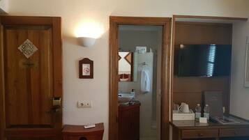 A hotel bathroom with a wooden door, a wall-mounted light, a framed sign, a mirror, a towel rack, a sink, and a television.