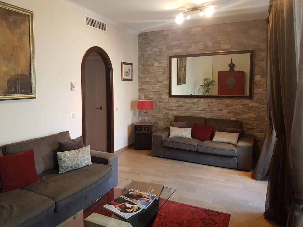 Un salon avec deux canapés, une table basse, un tapis rouge, un mur en pierre et un grand miroir.