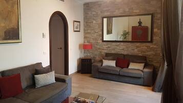 Una sala de estar con dos sofás, una mesa de centro, un tapete rojo, un muro de piedra y un espejo grande.
