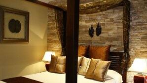 Una cama con dosel, un cabecero de pared de piedra, dos mesitas de noche con lámparas y un cuadro enmarcado en la pared.