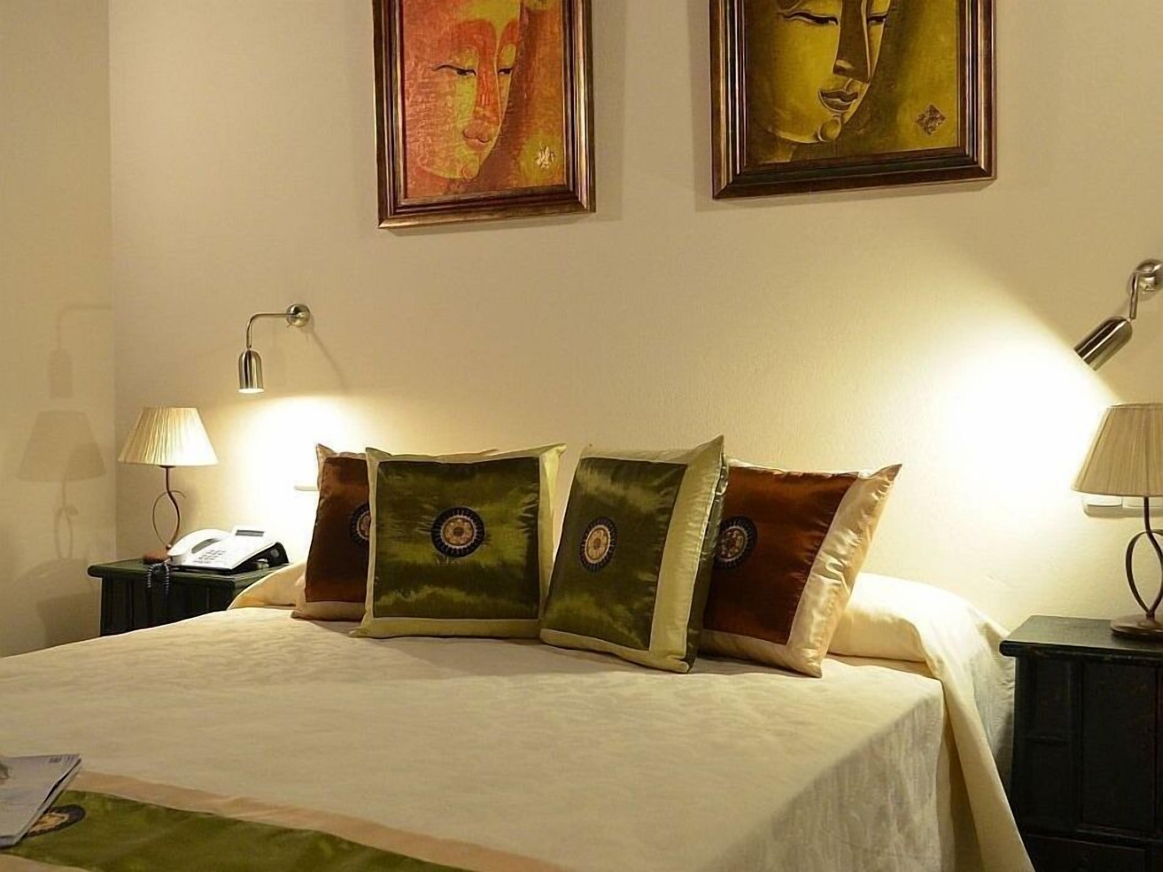 A neatly made bed with four decorative pillows, two bedside tables with lamps, and two framed artworks on the wall.
