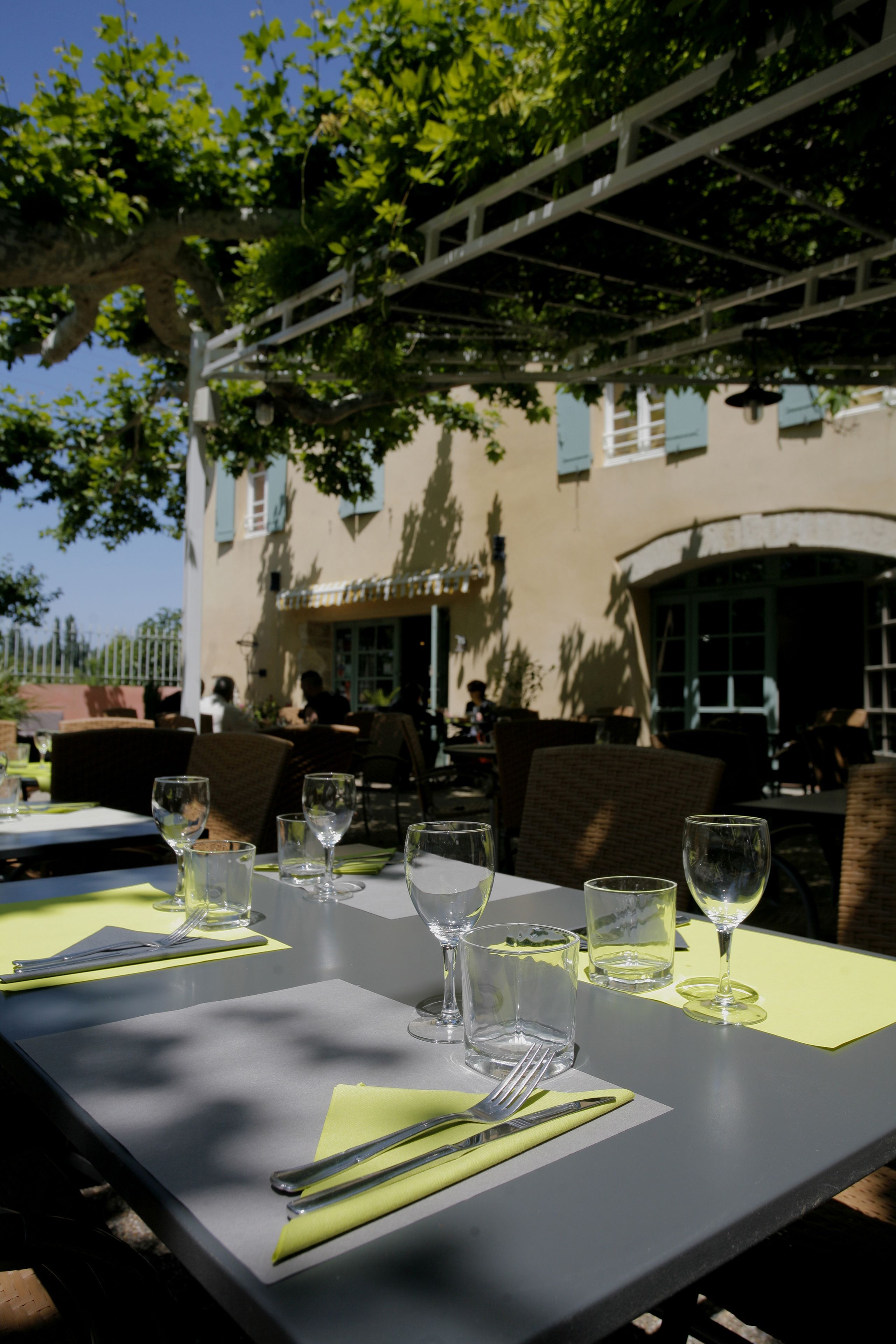 Un área de comedor al aire libre con mesas dispuestas para dos, con cubertería y copas de cristal.