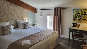 A bedroom with a stone wall, a bed with multiple pillows, a desk with a chair, and a painting on the wall. - Hotel Restaurant La Ferme (Avignon)