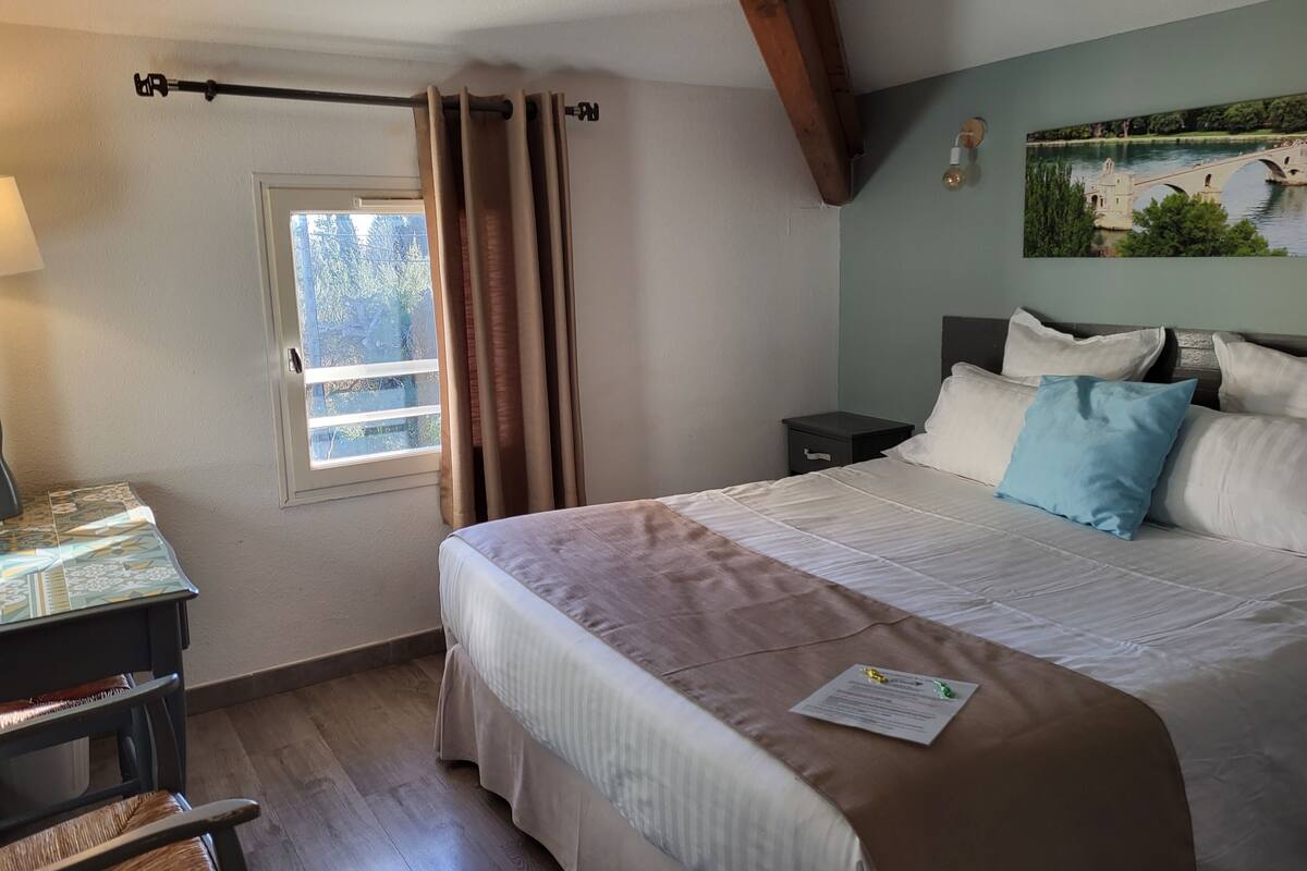 Une chambre bien rangée, avec un lit, une table de chevet et une fenêtre avec des rideaux.