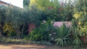 A garden with various plants and flowers, a wall, and a building in the background. - Hotel Restaurant La Ferme (Avignon)