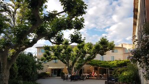 A courtyard with a gravel path, trees, outdoor seating, and bicycles. - Hotel Restaurant La Ferme (Avignon)