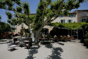 An outdoor seating area with tables and chairs, surrounded by potted plants and a large tree. - Hotel Restaurant La Ferme (Avignon)