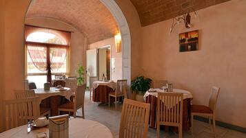 Zona pranzo con archi in mattoni, tavoli con tovaglioli bianchi e sedie.