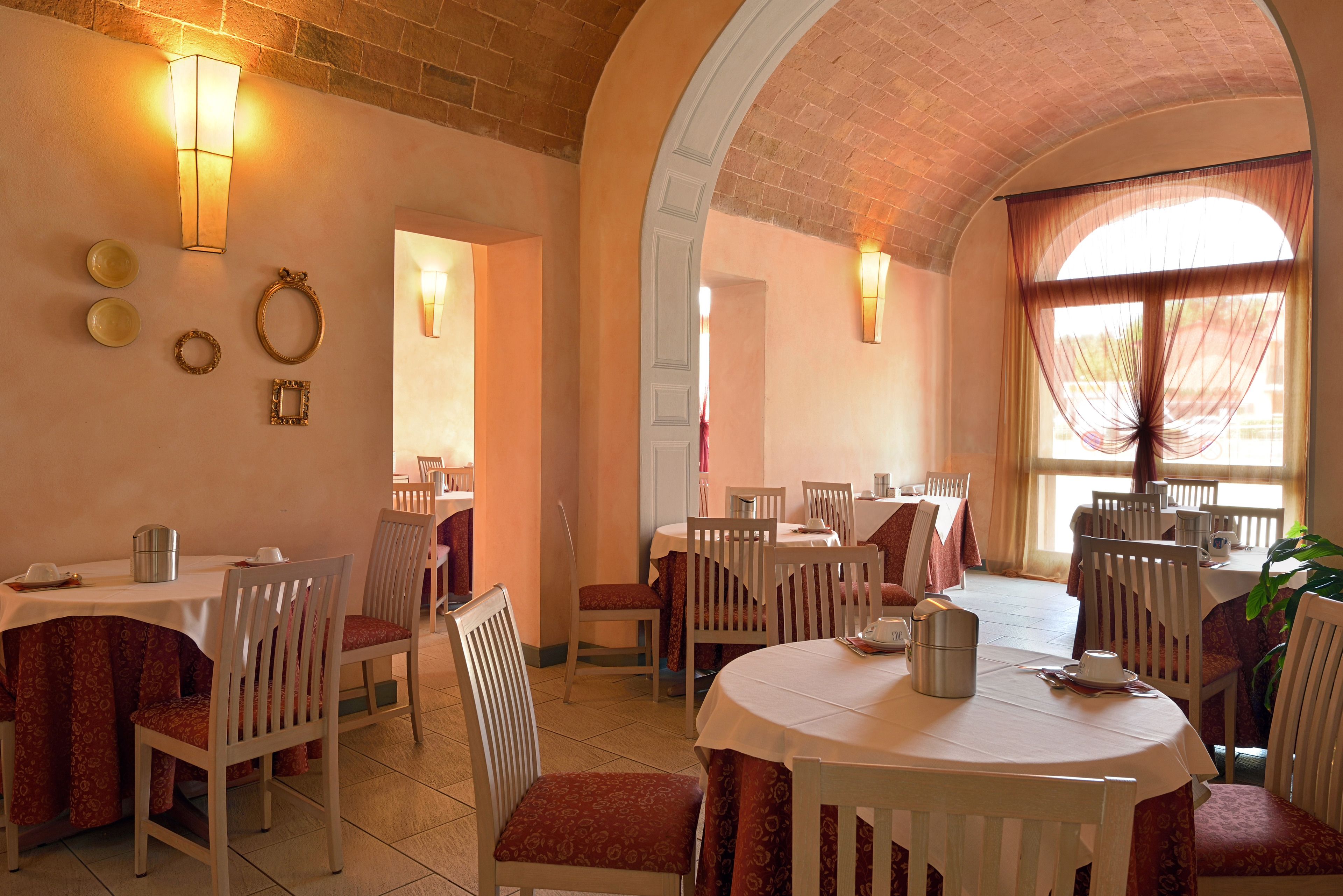 Zona pranzo con diversi tavoli e sedie, soffitto in mattoni e applique a parete.