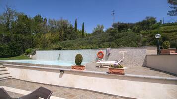 Zona de piscina exterior con un flotador salvavidas, sillas de descanso y plantas en macetas.
