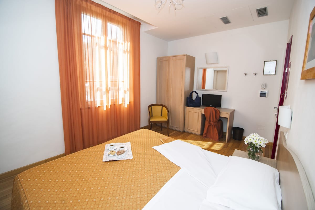 A hotel room with a bed, a desk, a chair, a wardrobe, and a window with curtains.