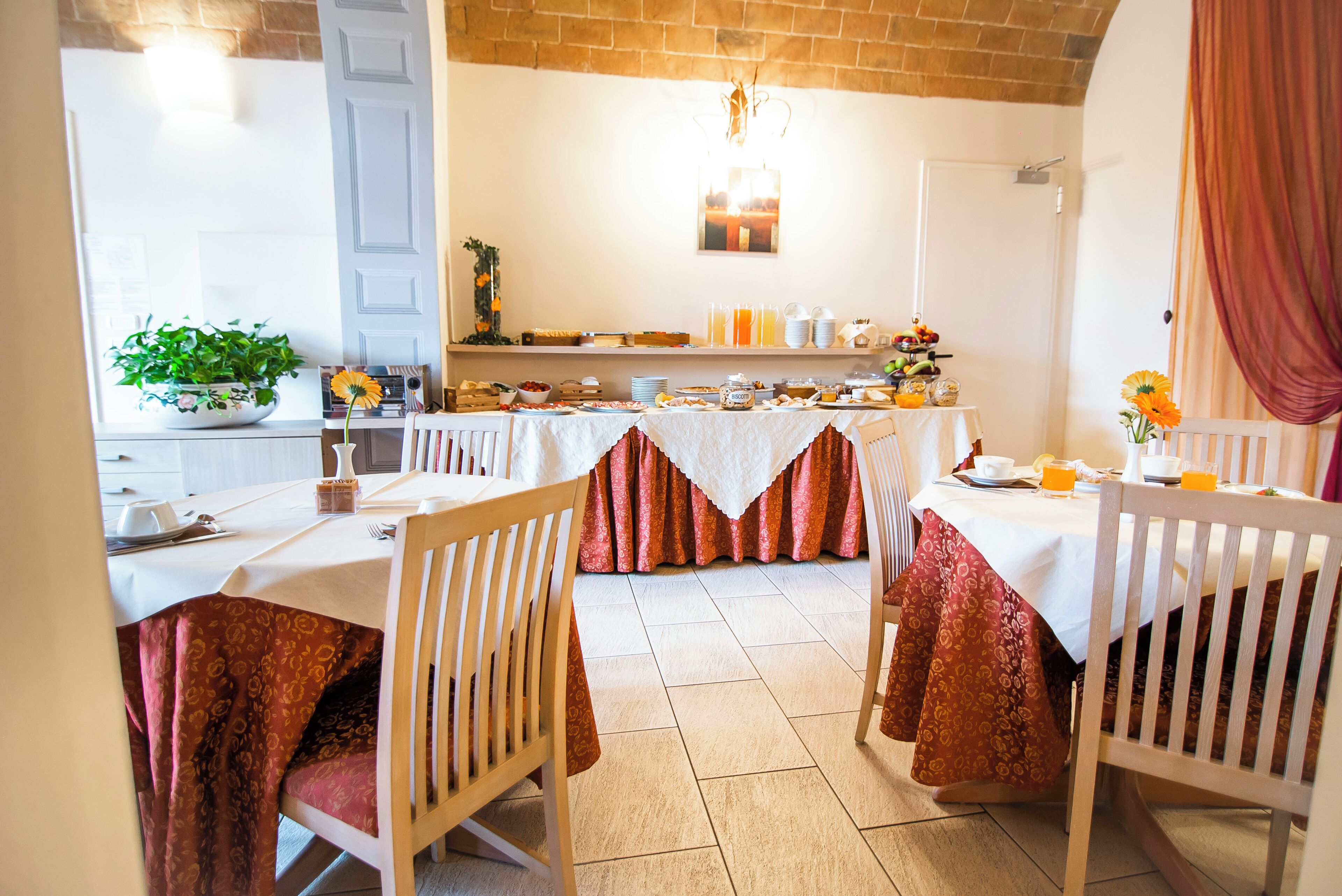 A dining area with tables set for breakfast, featuring a variety of food items and a decorative plant.