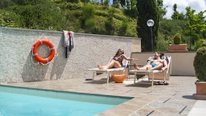 Zona junto a la piscina con sillones, un flotador salvavidas y una pared de piedra.