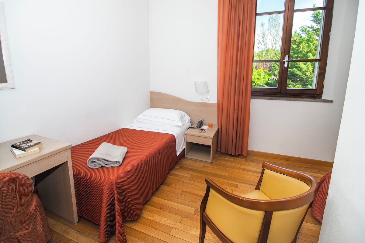 A hotel room with a bed, a desk, a chair, a nightstand, and a window with curtains.