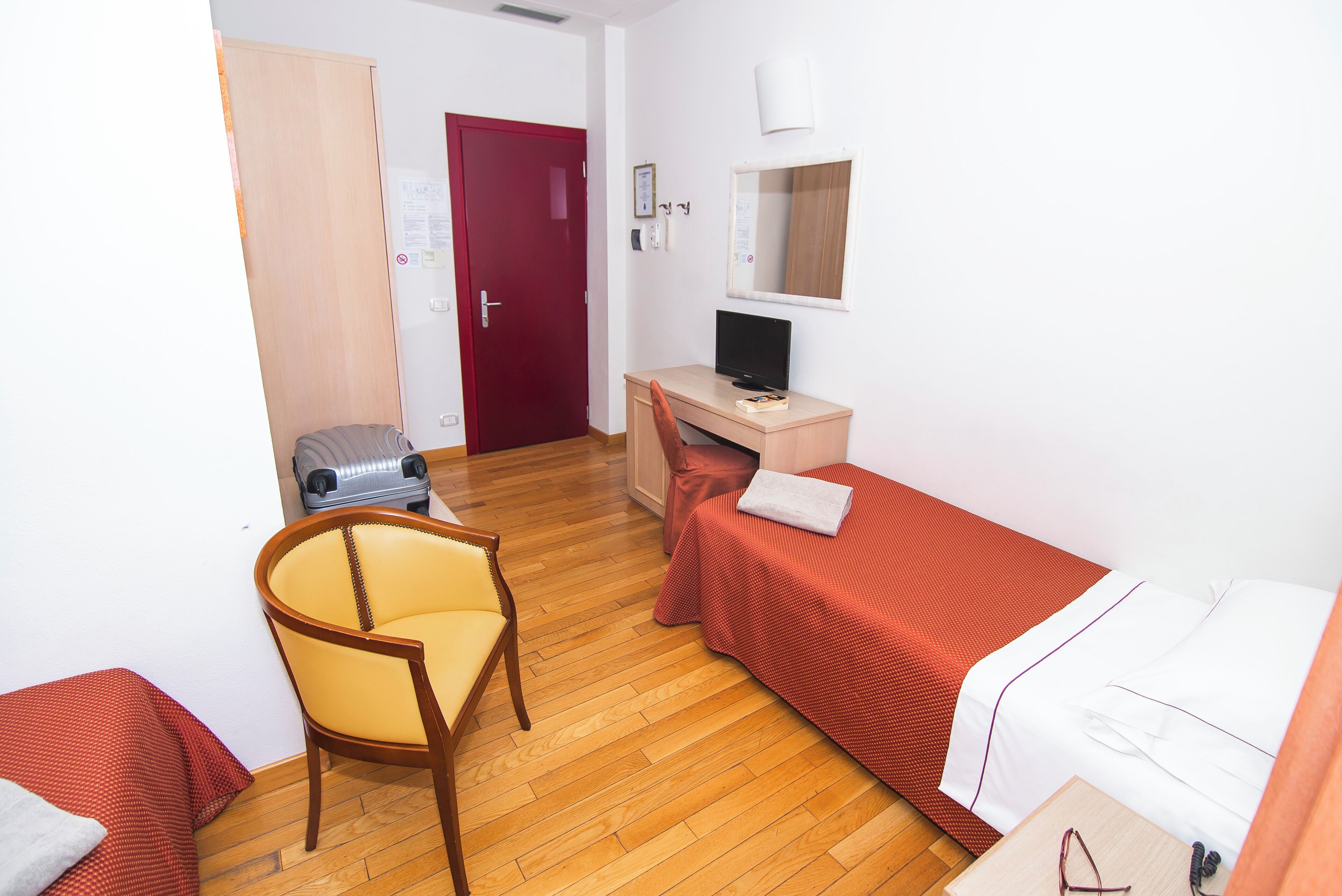 Habitación de hotel con suelo de madera, una cama individual, un escritorio con una computadora, una silla y un armario.