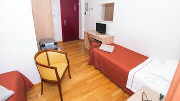 Habitación de hotel con suelo de madera, una cama individual, un escritorio con una computadora, una silla y un armario.