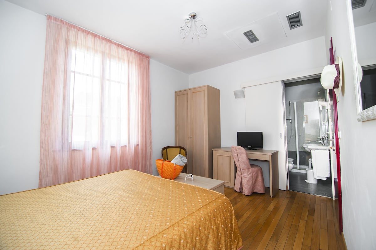 A bedroom with a bed, a desk, a chair, a wardrobe, and a bathroom visible through an open door.