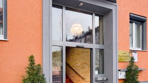 A hotel entrance with a glass door, a staircase inside, and two potted plants on either side. - Hotel Burgschmiet (Nuremberg)