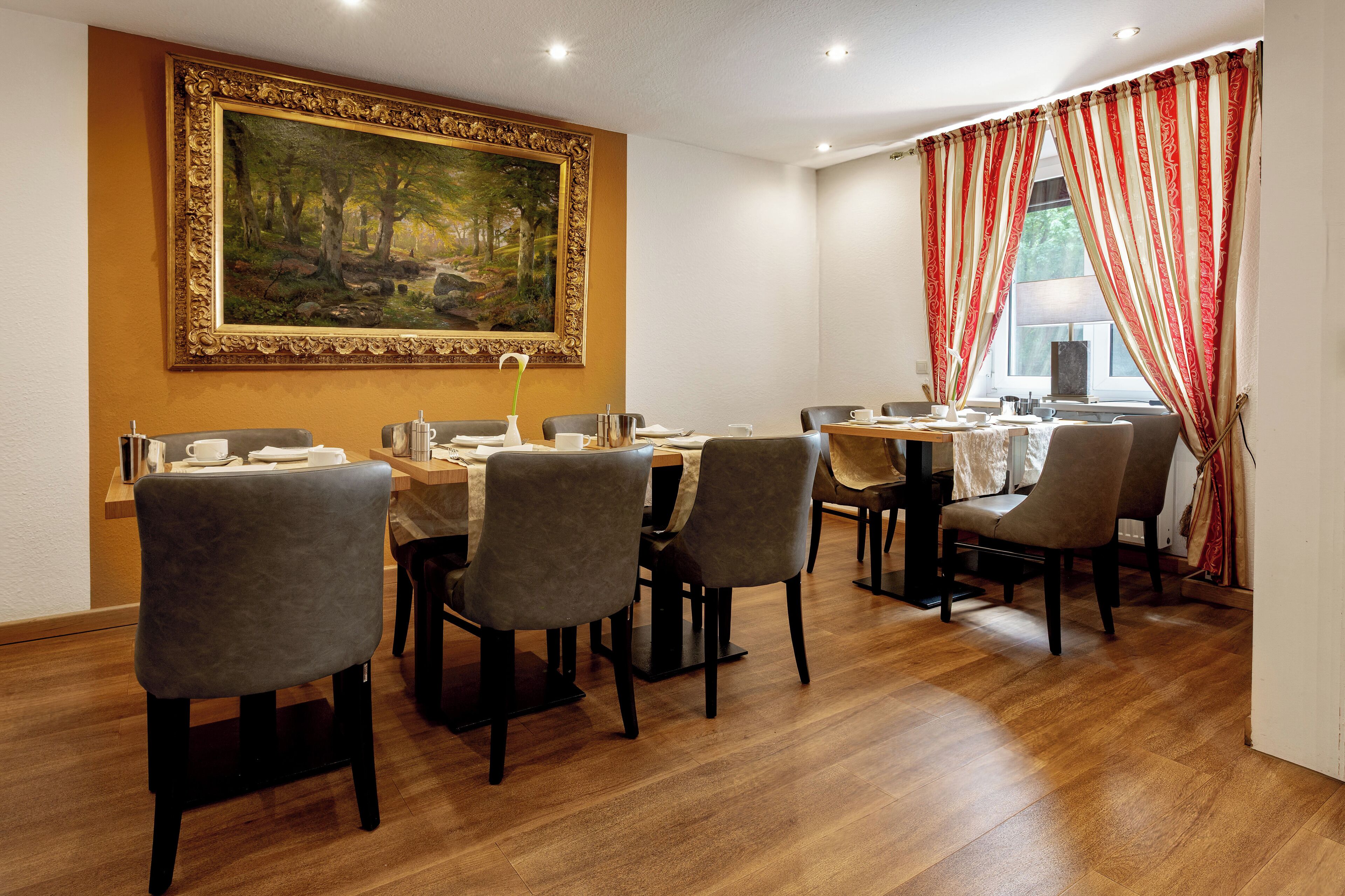A dining area with a large painting on the wall, a wooden table, and grey upholstered chairs.