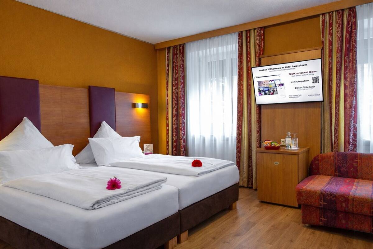 A hotel room with two beds, a TV, a small table, and a chair.