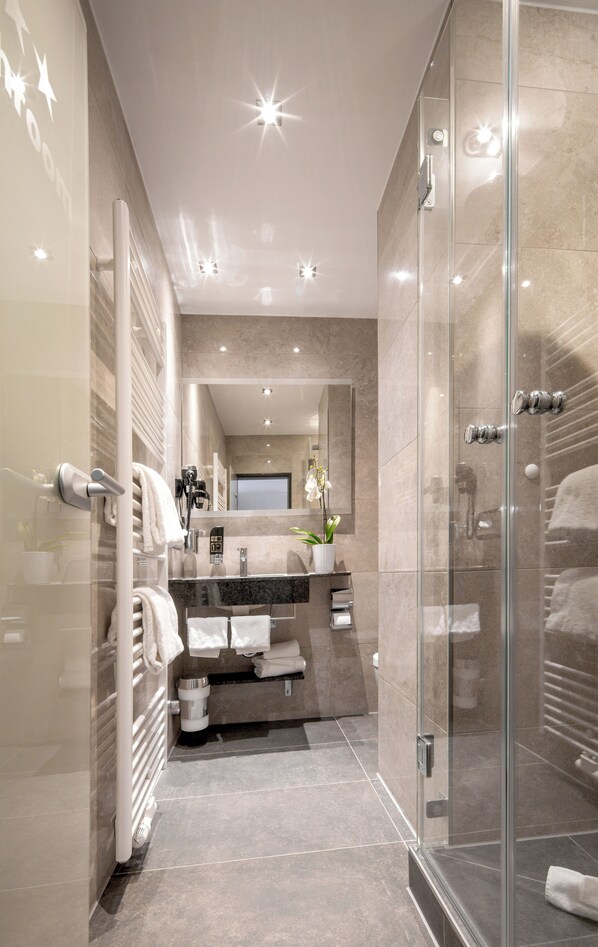 A modern bathroom with a glass shower enclosure, a vanity with a mirror, and a towel rack. - Hotel Burgschmiet (Nuremberg)