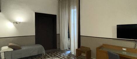 A hotel room with a bed, a desk, a chair, a television, and a bathroom door.