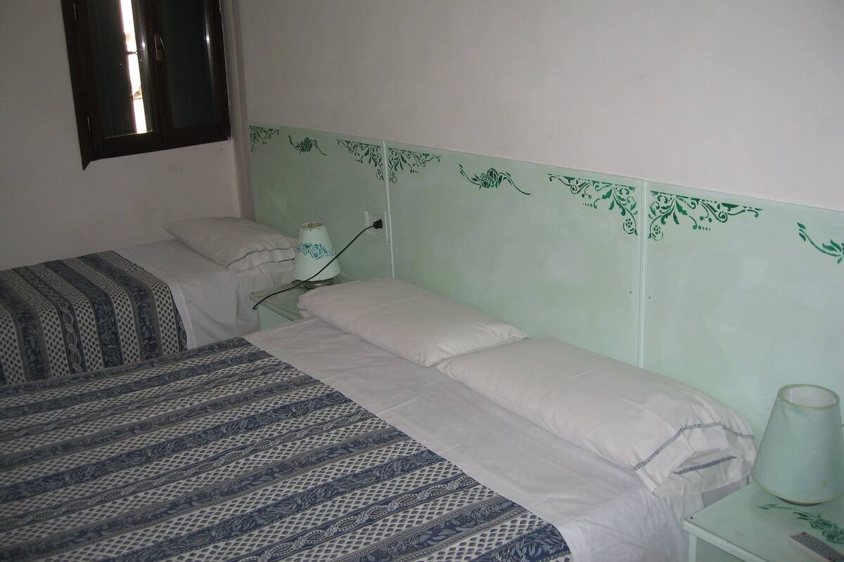 A room with two beds, a nightstand, a lamp, and a window.