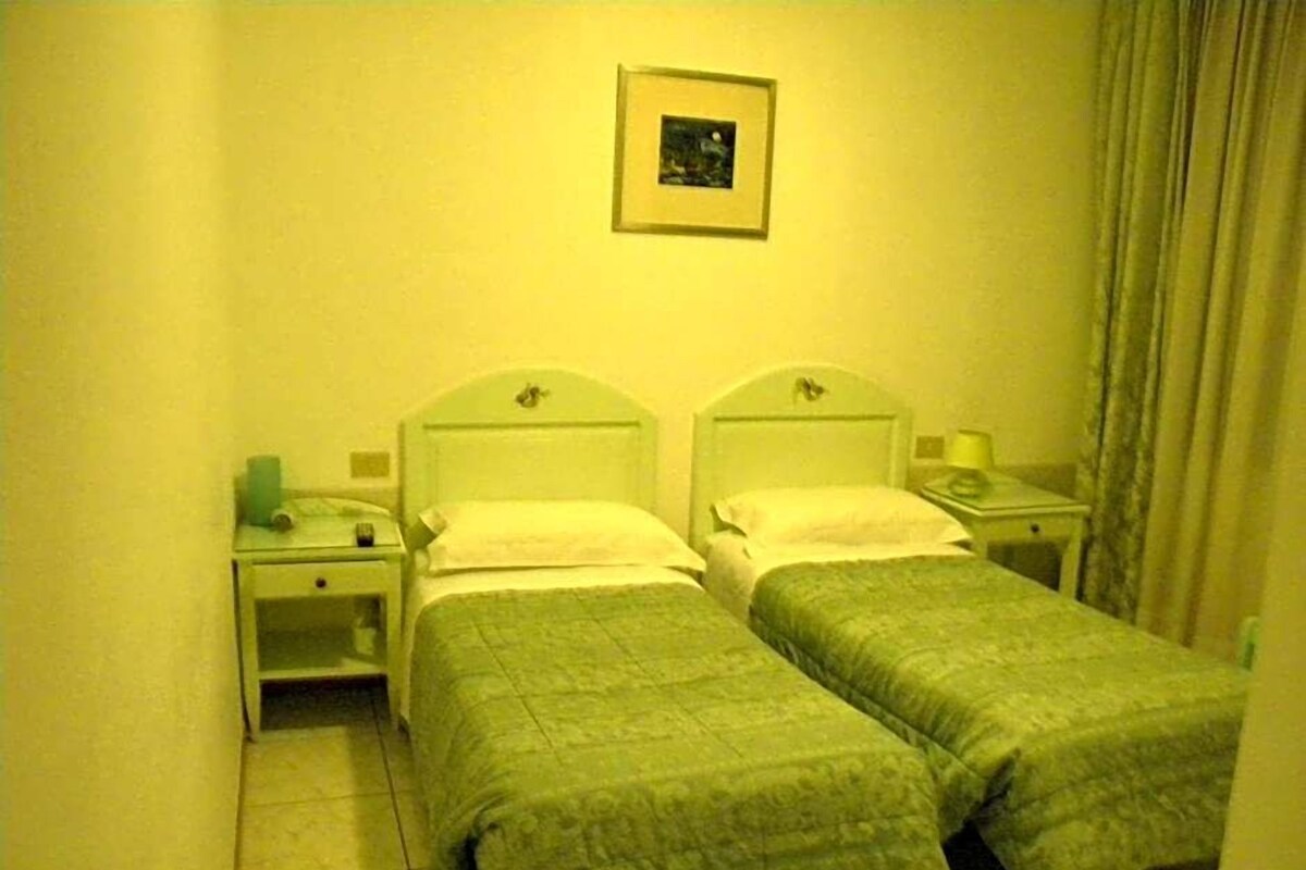 A room with two single beds, a nightstand with a lamp, and a framed picture on the wall.