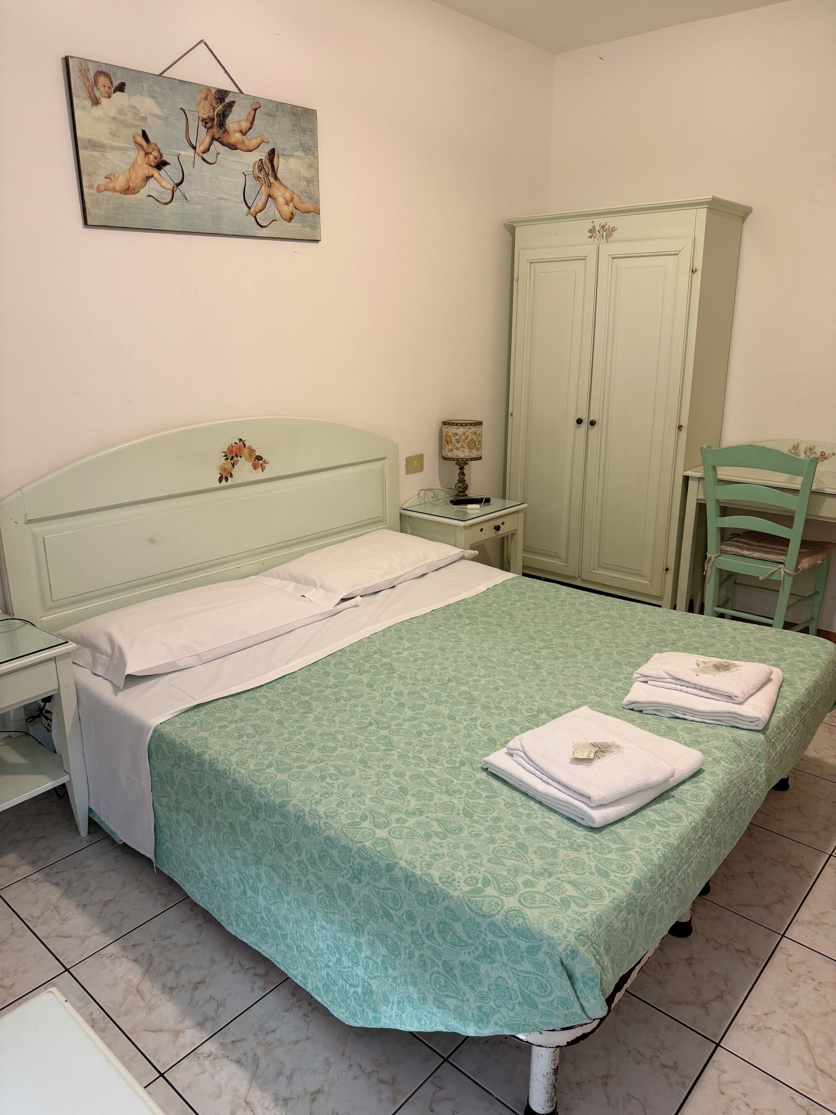 A bedroom with a bed, nightstand, lamp, wardrobe, and a chair.