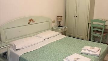 Ein Schlafzimmer mit Bett, Nachttisch, Lampe, Kleiderschrank und einem Sessel.