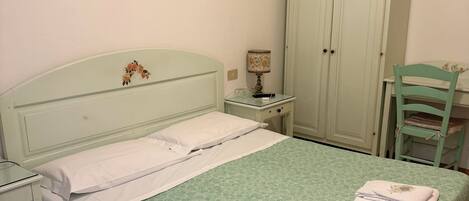 A bedroom with a bed, nightstand, lamp, wardrobe, and a chair.