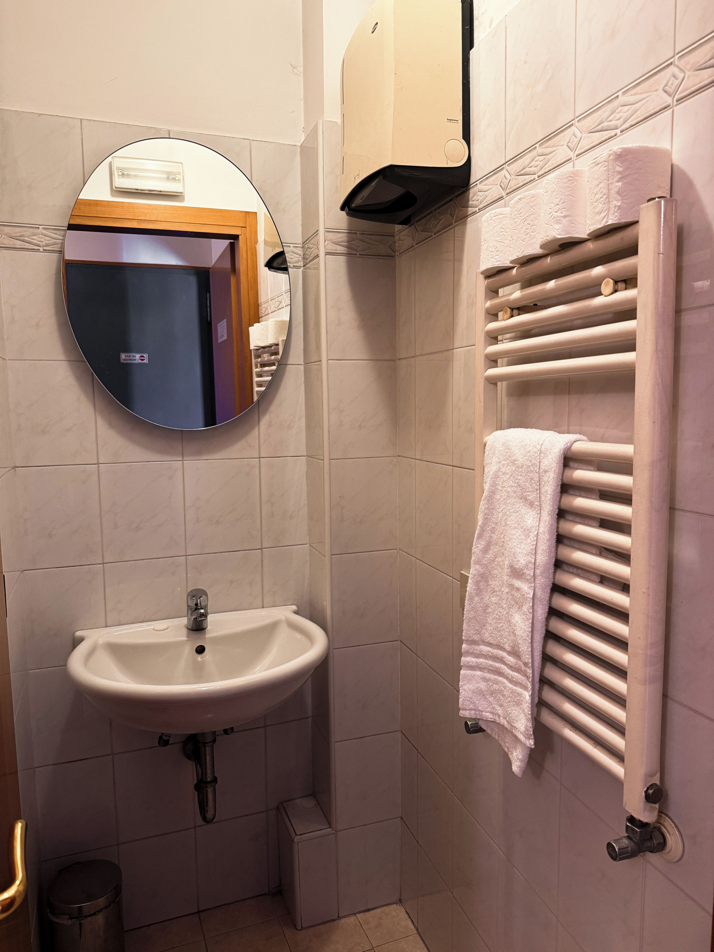 Une salle de bain équipée d’un lavabo, d’un miroir, d’un porte-serviettes et d’une poubelle.