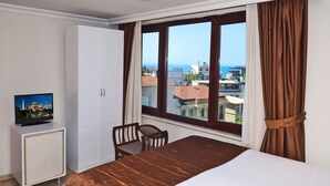 A hotel room with a bed, a desk with a TV, a wardrobe, and a window with a view of buildings and the sea. - Sunrise Hotel (Istanbul)