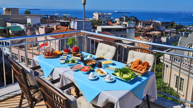 A balcony with a table set for a meal, overlooking a cityscape with buildings and the sea. - Sunrise Hotel (Istanbul)