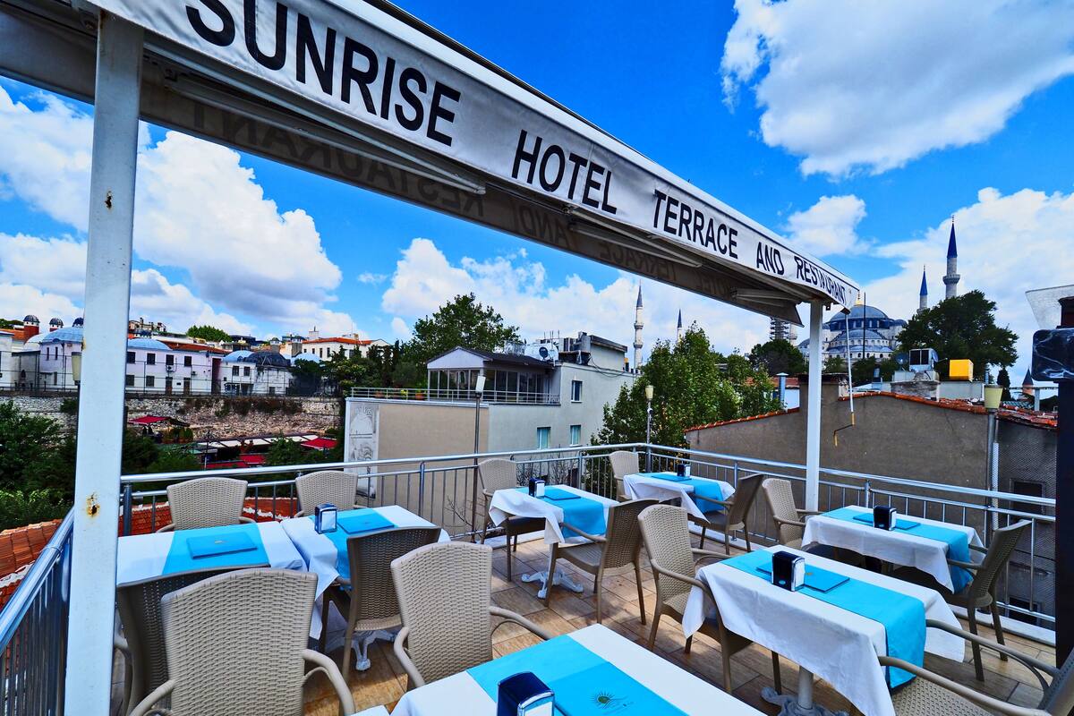 A terrace at Sunrise Hotel with tables and chairs, overlooking a cityscape with historical buildings and a mosque.