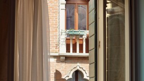 An open window with a view of a brick building, a balcony, and a curtain partially drawn. - Hotel Tiepolo (Venice)