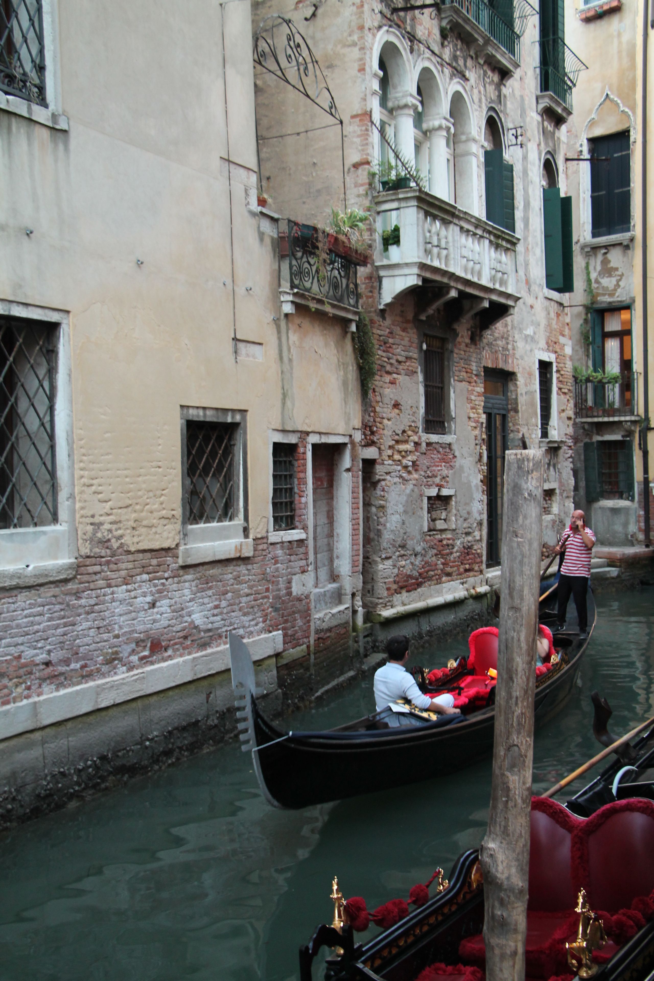 A canal with gondolas, a wooden post, and a building with a balcony.