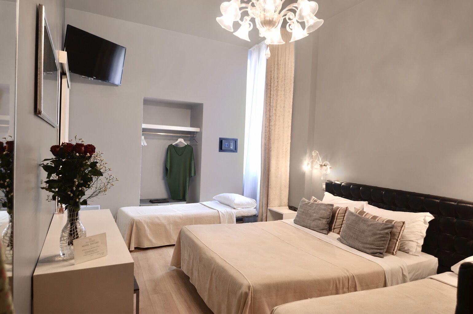 Een hotelkamer met twee bedden, een televisie, een kroonluchter, een spiegel en een vaas met bloemen.